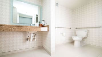 A bathroom with a sink, mirror, toilet, and grab bars.