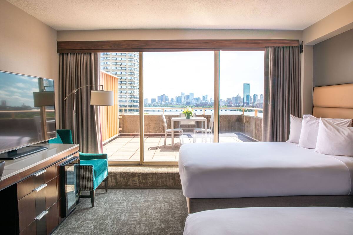 Habitación de hotel con una cama grande, un escritorio con televisor, un balcón con vista a la ciudad y un comedor.