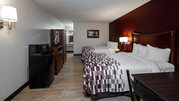 A hotel room with a large bed, a desk, a chair, a television, and a wardrobe.
