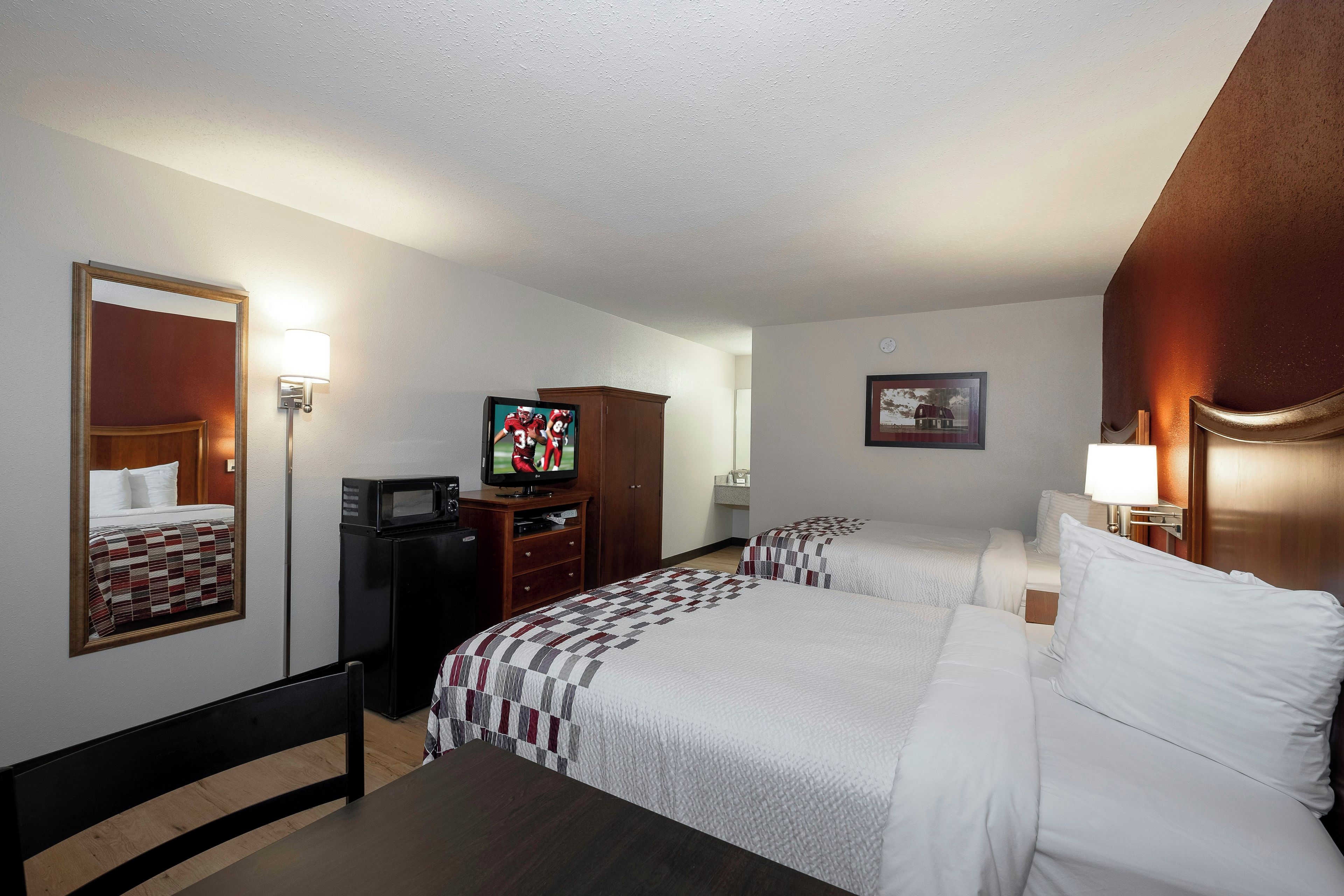 A hotel room with two beds, a television, a desk, a mirror, and a picture on the wall.