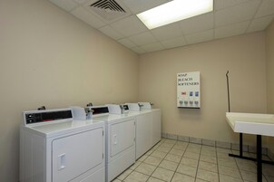 A laundry room with multiple washing machines and dryers, a sign indicating softener options, and a tiled floor.