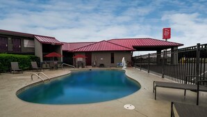 A hotel with a swimming pool, outdoor seating, and a fenced patio area.