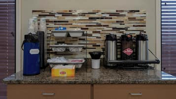 A coffee station with a coffee maker, hot water dispenser, and a box of napkins.