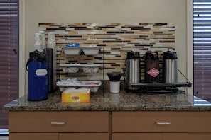Cantinho com café, máquina de café, dispensador de água quente e caixa de guardanapos.