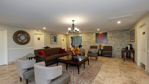 A spacious living area with a brown sofa, grey armchairs, a coffee table, and a patterned rug. - Red Roof Inn Dothan (Dothan)