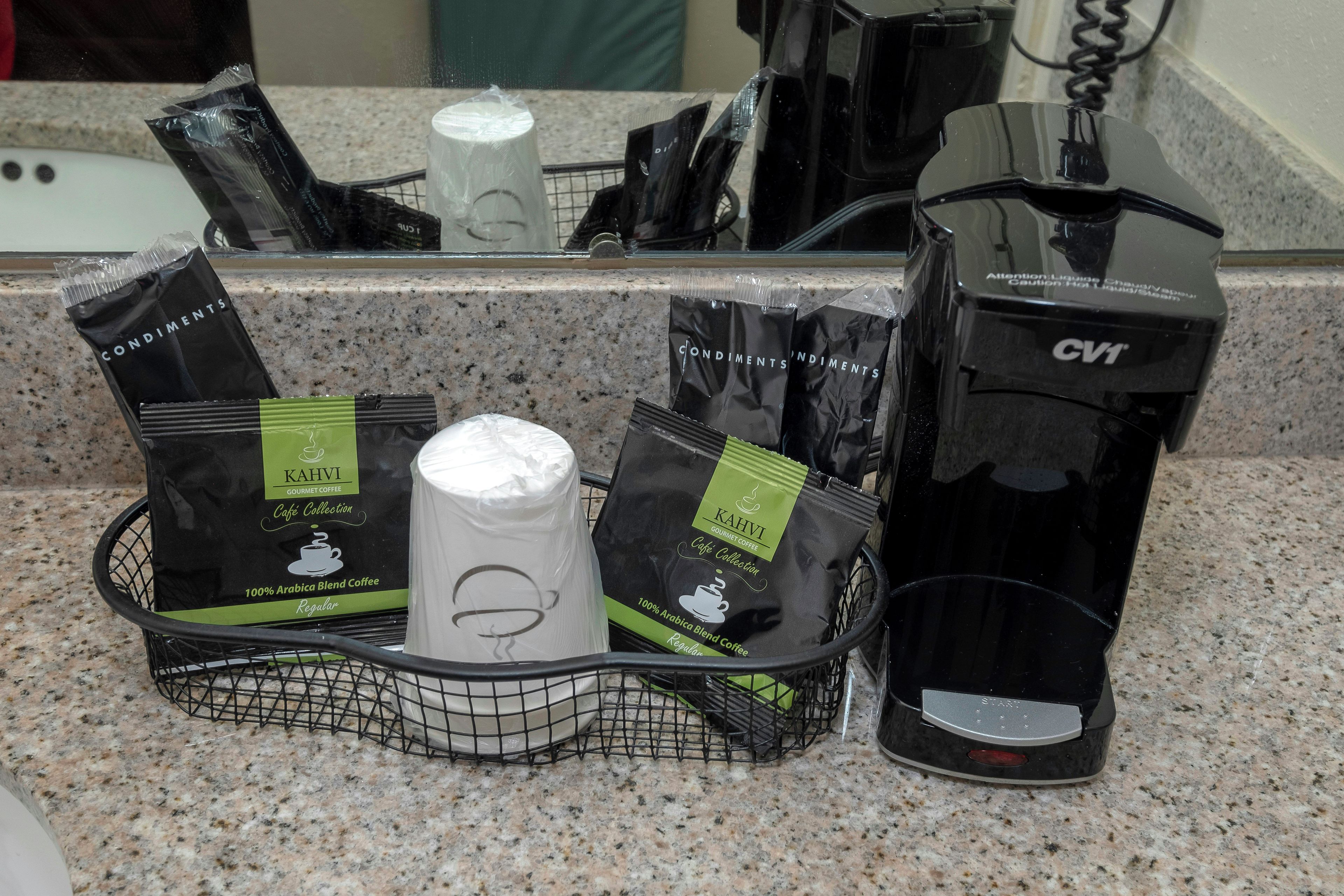 A coffee machine, a coffee maker, and a basket with coffee pods and a coffee cup on a kitchen counter.