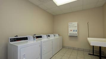 Un cuarto de lavandería con varias lavadoras y secadoras, un cartel que indica la disponibilidad de suavizante, y un piso de baldosas.