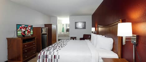 A hotel room with a bed, a TV, a desk, a dresser, and a bathroom visible in the background.