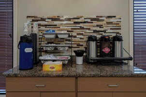 A coffee station with a coffee machine, hot water dispenser, and disposable cups.