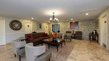 A spacious living room with a brown sofa, grey armchairs, a coffee table, and a patterned rug.