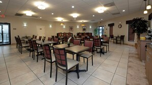 A spacious dining area with multiple tables and chairs, ceiling lights, and a clock on the wall.
