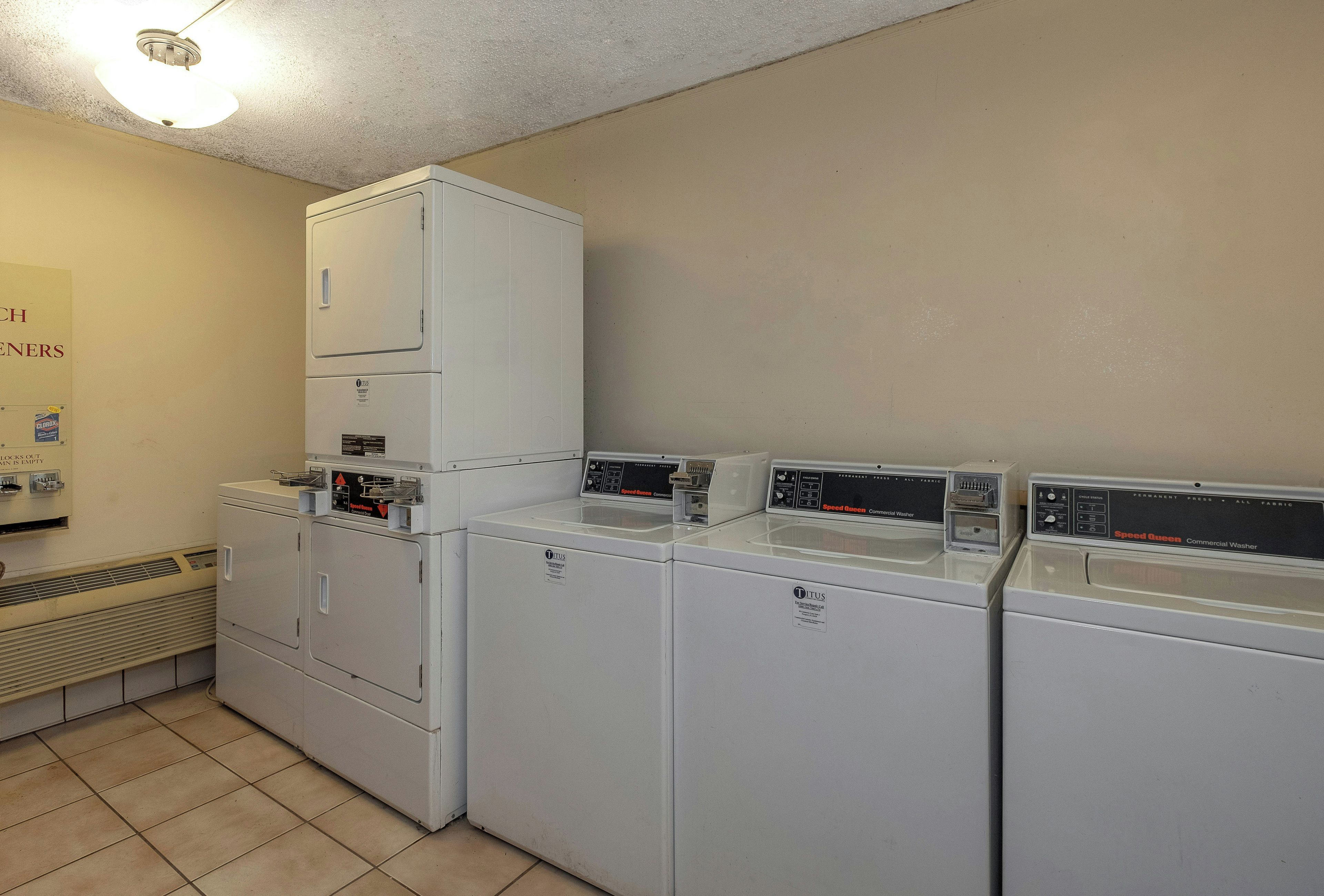 A laundry facility with multiple washing machines and dryers, a vent system, and a sign indicating the location.