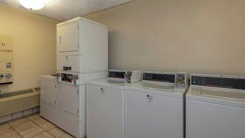 A laundry facility with multiple washing machines and dryers, a vent system, and a sign indicating the location.