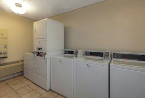 Un cuarto de lavandería con varias lavadoras y secadoras, un sistema de ventilación y un cartel que indica la ubicación.