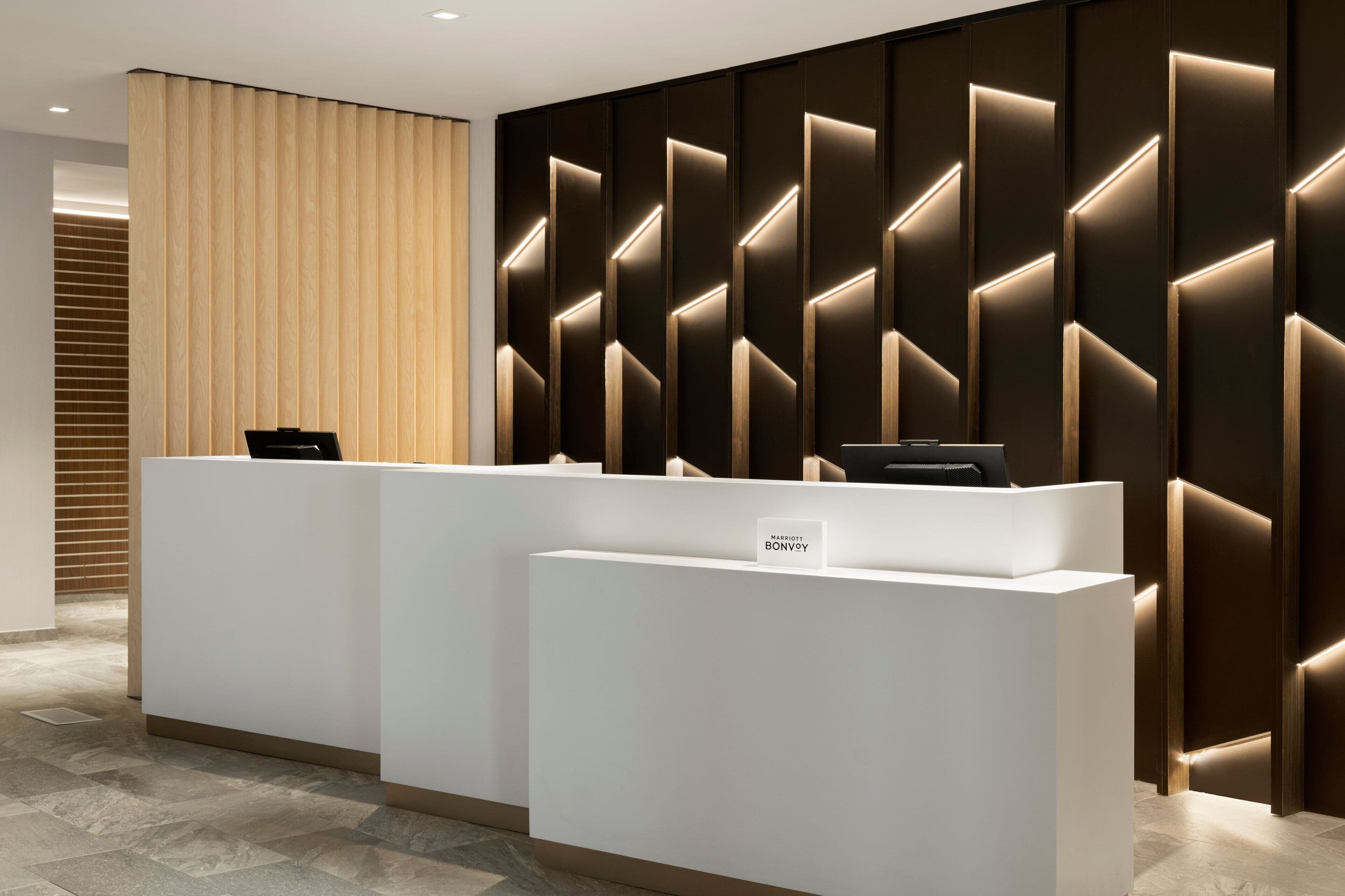 A reception area with a modern design, featuring a reception desk and a wall with geometric lighting.