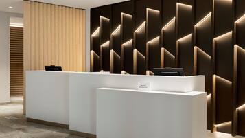 A reception area with a modern design, featuring a reception desk and a wall with geometric lighting.