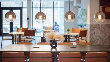 A modern dining area with round tables and orange chairs, large windows, and hanging spherical light fixtures.