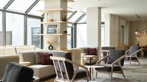 A modern living room with a sofa, armchairs, and a coffee table. There is a bookshelf with decorative items and a large window providing natural light. - AC Hotel Frisco Colorado (Frisco)