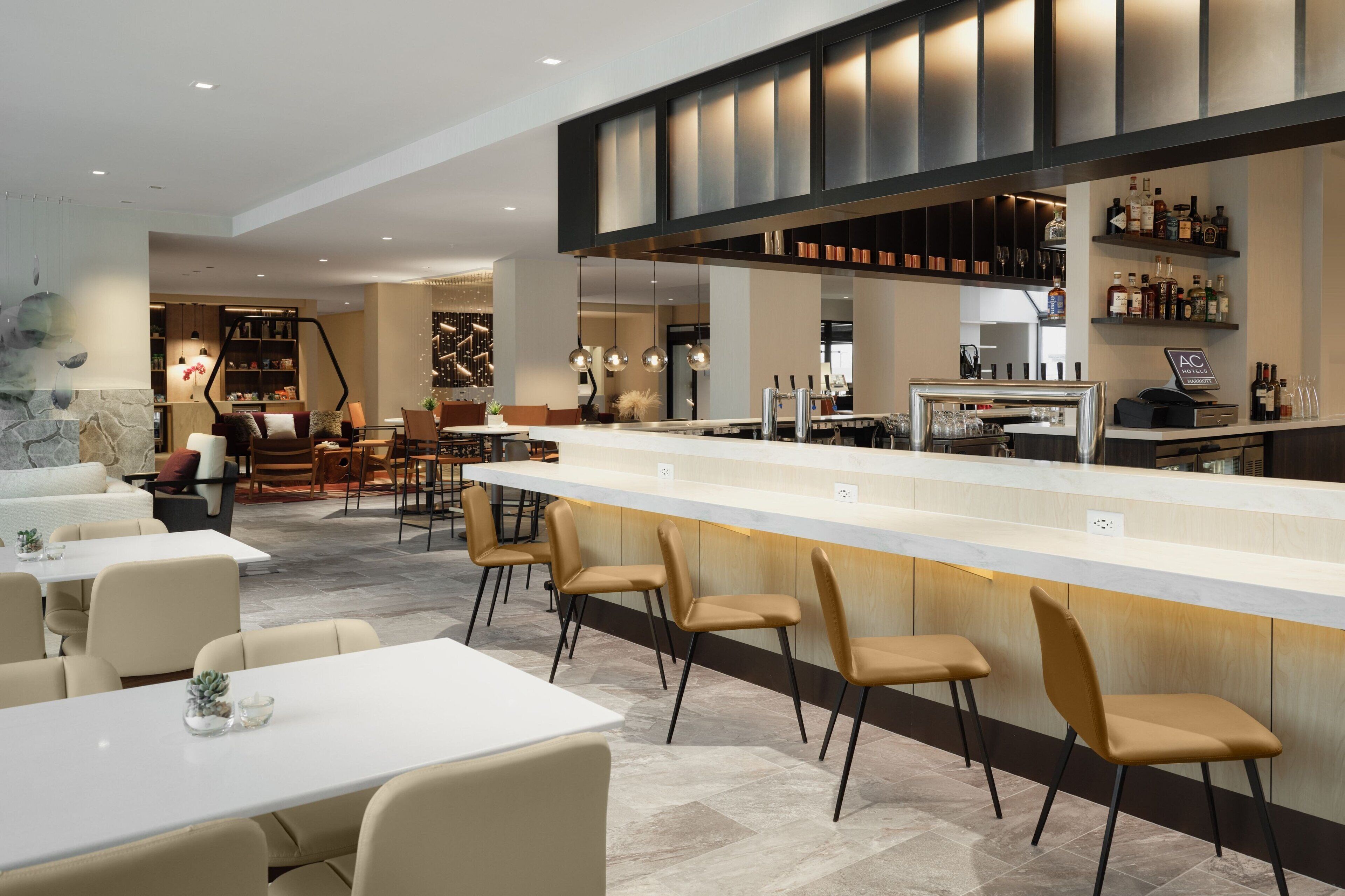 Zona de bar moderna con una barra larga, taburetes y una variedad de botellas y vasos.