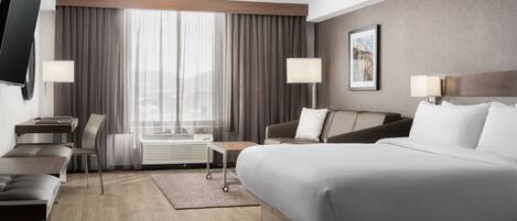 A modern hotel room with a large bed, a desk, a chair, a TV, and a window with curtains.