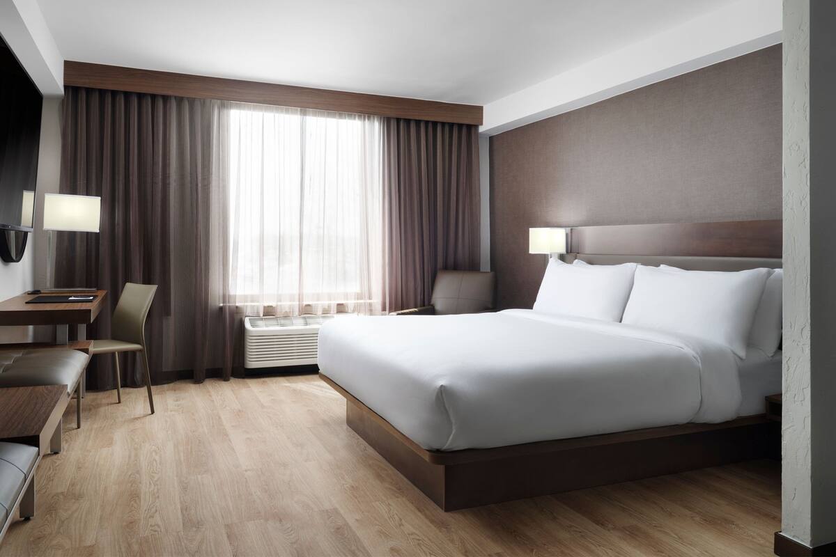 A hotel room with a large bed, a desk, a chair, and a window with curtains.