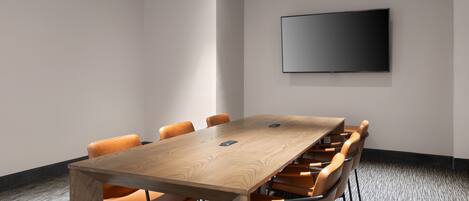 A conference room with a wooden table and orange chairs, a flat-screen TV on the wall, and carpeted flooring.