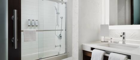 Ein modernes Badezimmer mit einer gläsernen Duschkabine, einem weißen Waschbecken und einem Spiegel darüber.
