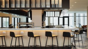 A modern bar area with a long counter, multiple stools, and a large window providing natural light. - AC Hotel Frisco Colorado (Frisco)