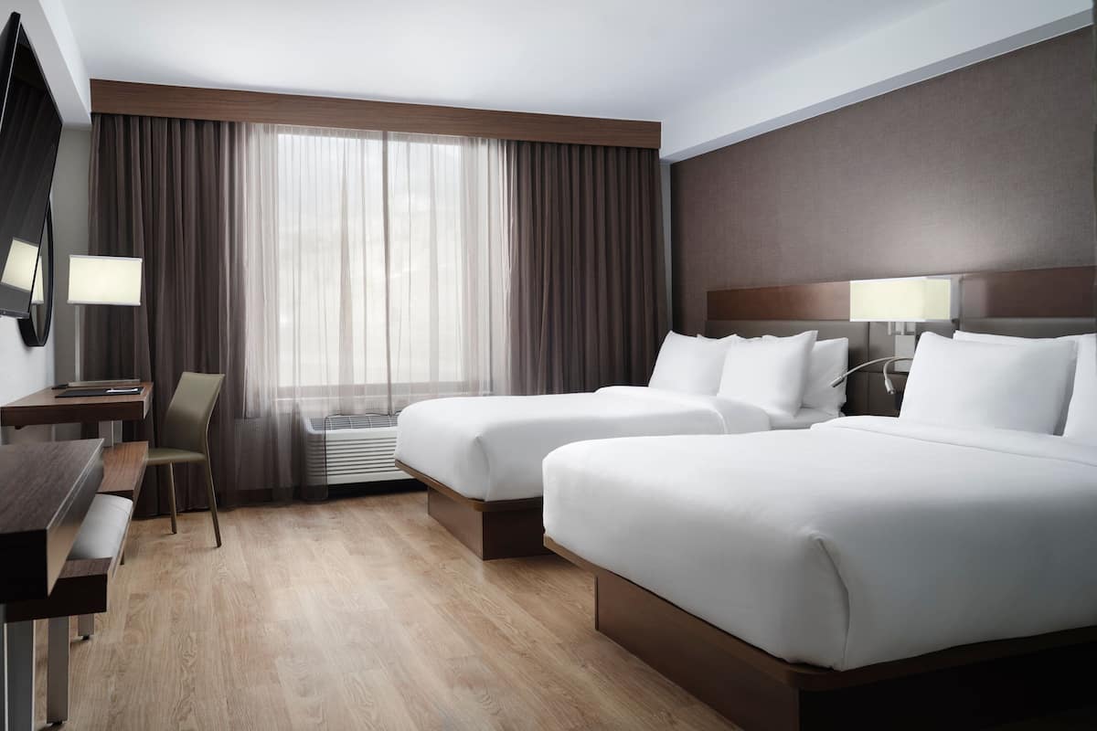 A hotel room with two beds, a desk, a chair, and a TV.