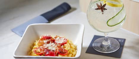 A white bowl of pasta with cherry tomatoes and a glass of water with lemon slices and a star anise.