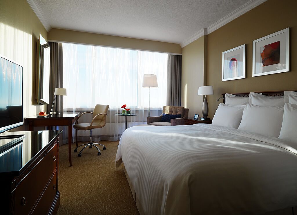 A hotel room with a large bed, a desk with a chair, a TV, and two lamps.
