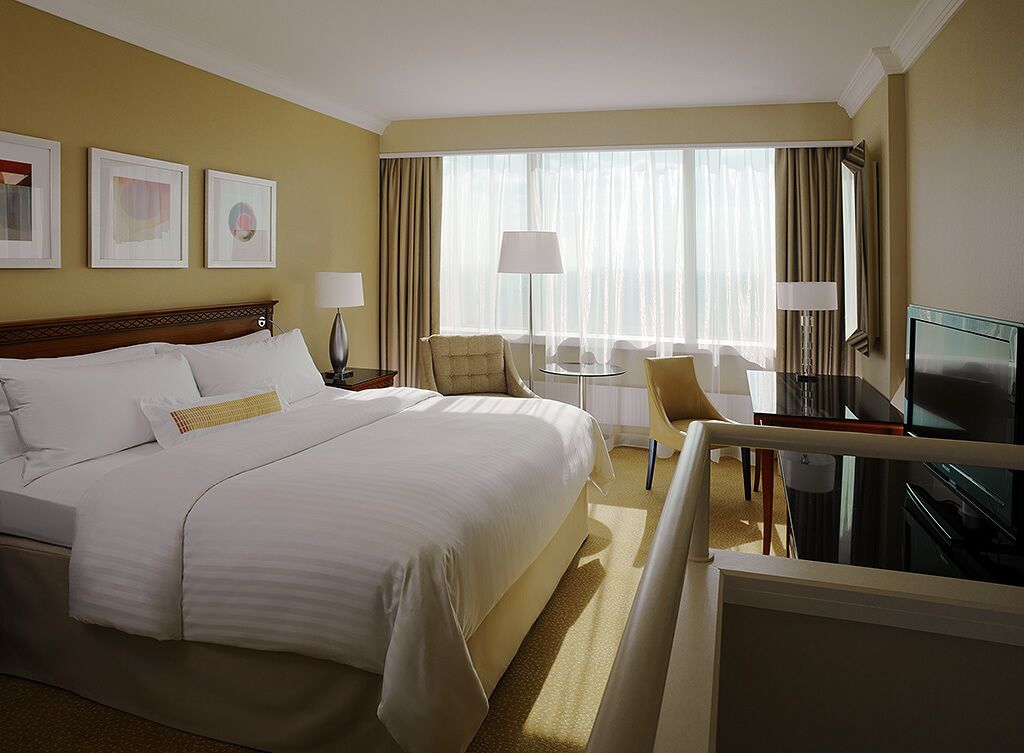 A hotel room with a large bed, two chairs, a small table, a TV, and a window with curtains.