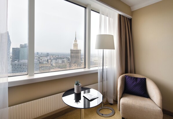 Une chambre d’hôtel dotée d’une grande fenêtre donnant sur la ville, d’une table ronde avec une lampe et d’un fauteuil confortable.