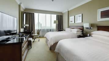 Ein Hotelzimmer mit zwei Betten, einem Schreibtisch mit Computer, einem Stuhl und einem Vorhangfenster.