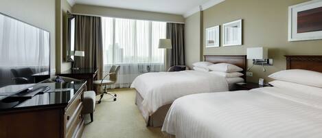 A hotel room with two beds, a desk with a computer, a chair, and a window with curtains.