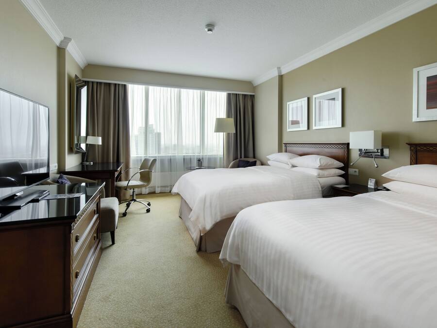 A hotel room with two beds, a desk with a computer, a chair, and a window with curtains.
