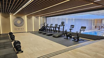 Ein Fitnessstudio mit Laufbändern, Crosstrainern und Rudergerät, mit einem großen Fenster mit Blick auf ein Schwimmbecken.