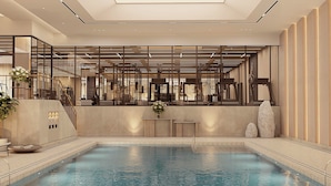 Area piscina interna moderna con vista chiara sulla vasca, una reception e una scala che conduce ai piani superiori.