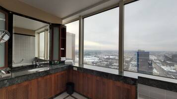 A modern bathroom with a large mirror, two sinks, and a view of a cityscape through large windows.