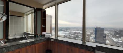 A modern bathroom with a large mirror, two sinks, and a view of a cityscape through large windows.