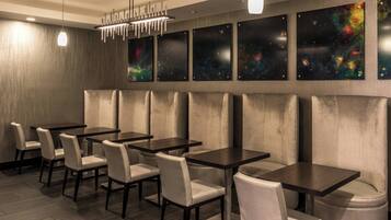 Un restaurante con mesas y sillas de madera oscura, un candelabro moderno y arte mural con temática de galaxia.