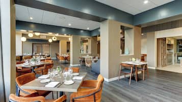 A modern dining area with multiple tables and chairs, a kitchen area, and a view of the dining space.