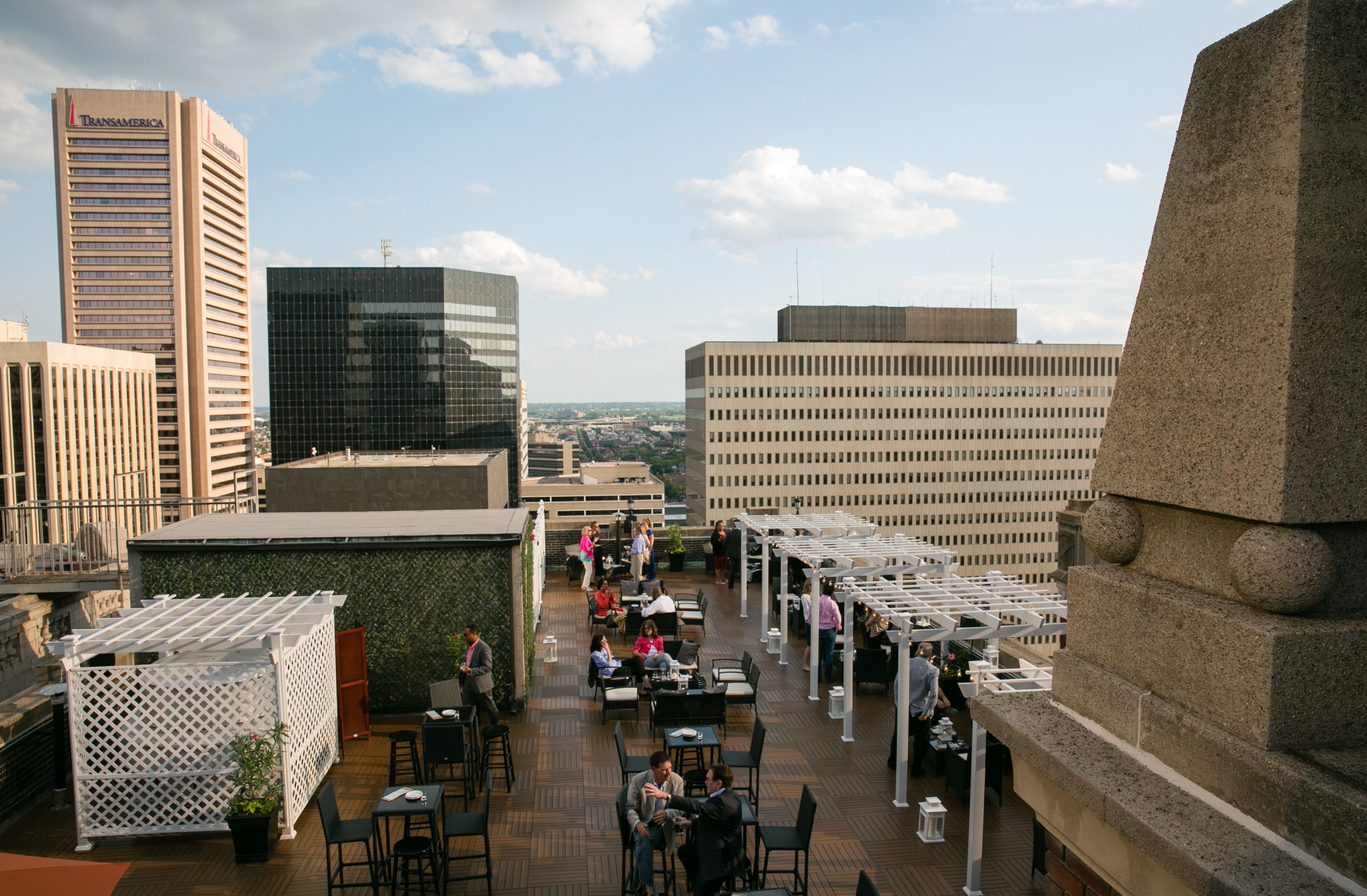 A rooftop terrace with outdoor seating, a view of city buildings, and a clear sky.