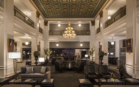 A spacious lobby with a grand chandelier, multiple seating areas, and a piano in the background.