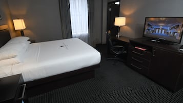 A hotel room with a large bed, a desk with a chair, a television, and a dresser.