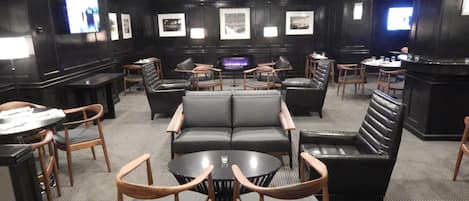 A modern lounge area with leather sofas, wooden chairs, and a central table.