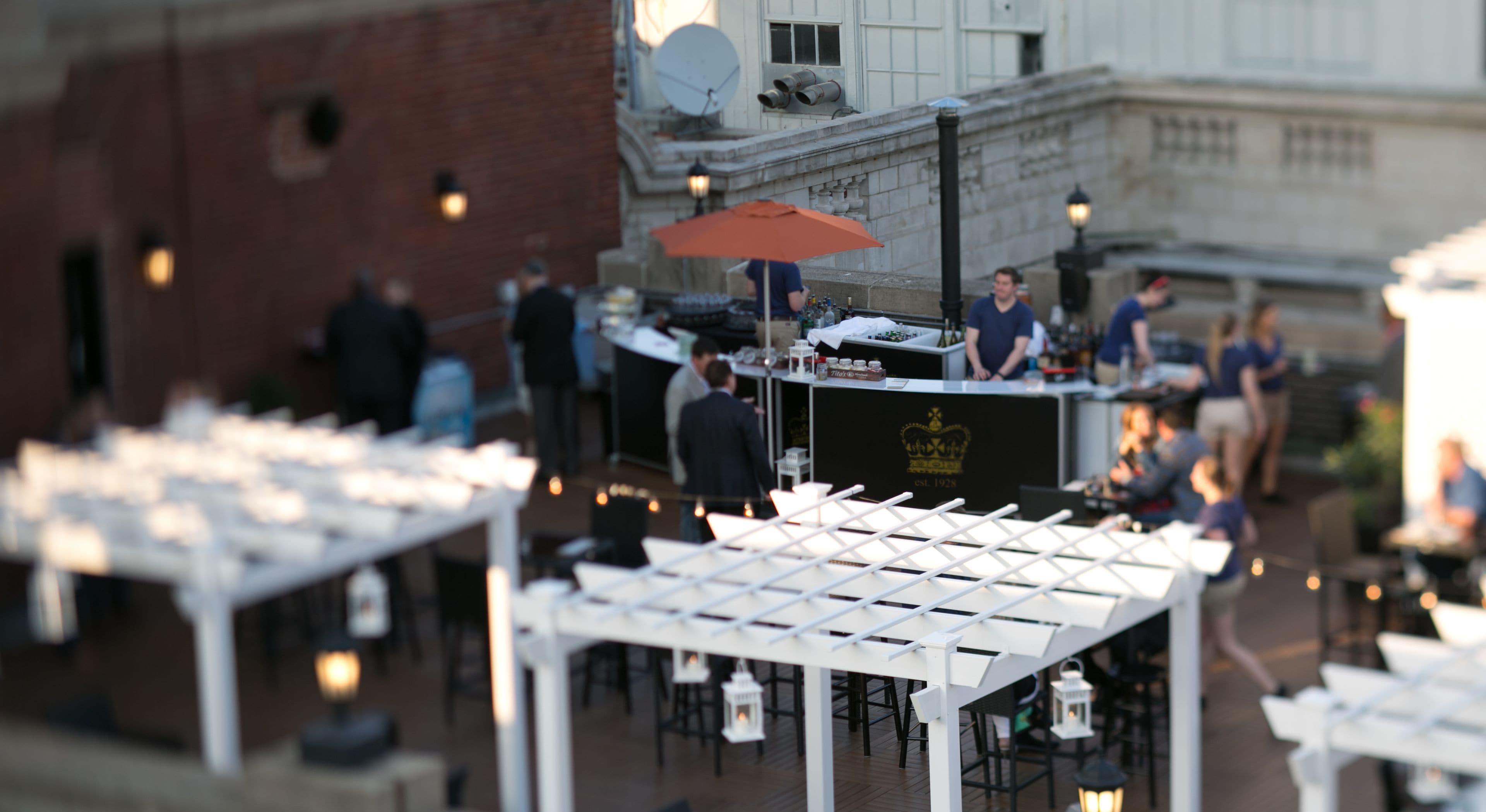 Outdoor seating with tables and chairs, a bar area with a counter, and a building with classical architecture in the background.