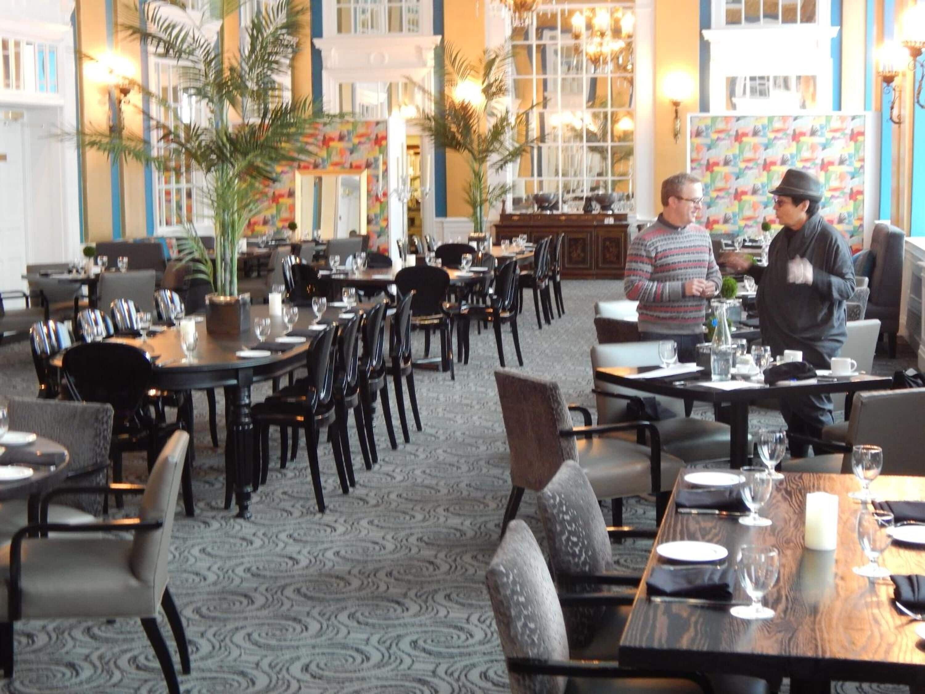 A spacious restaurant with multiple tables and chairs, a patterned carpet, and a decorative wall with a colorful pattern.