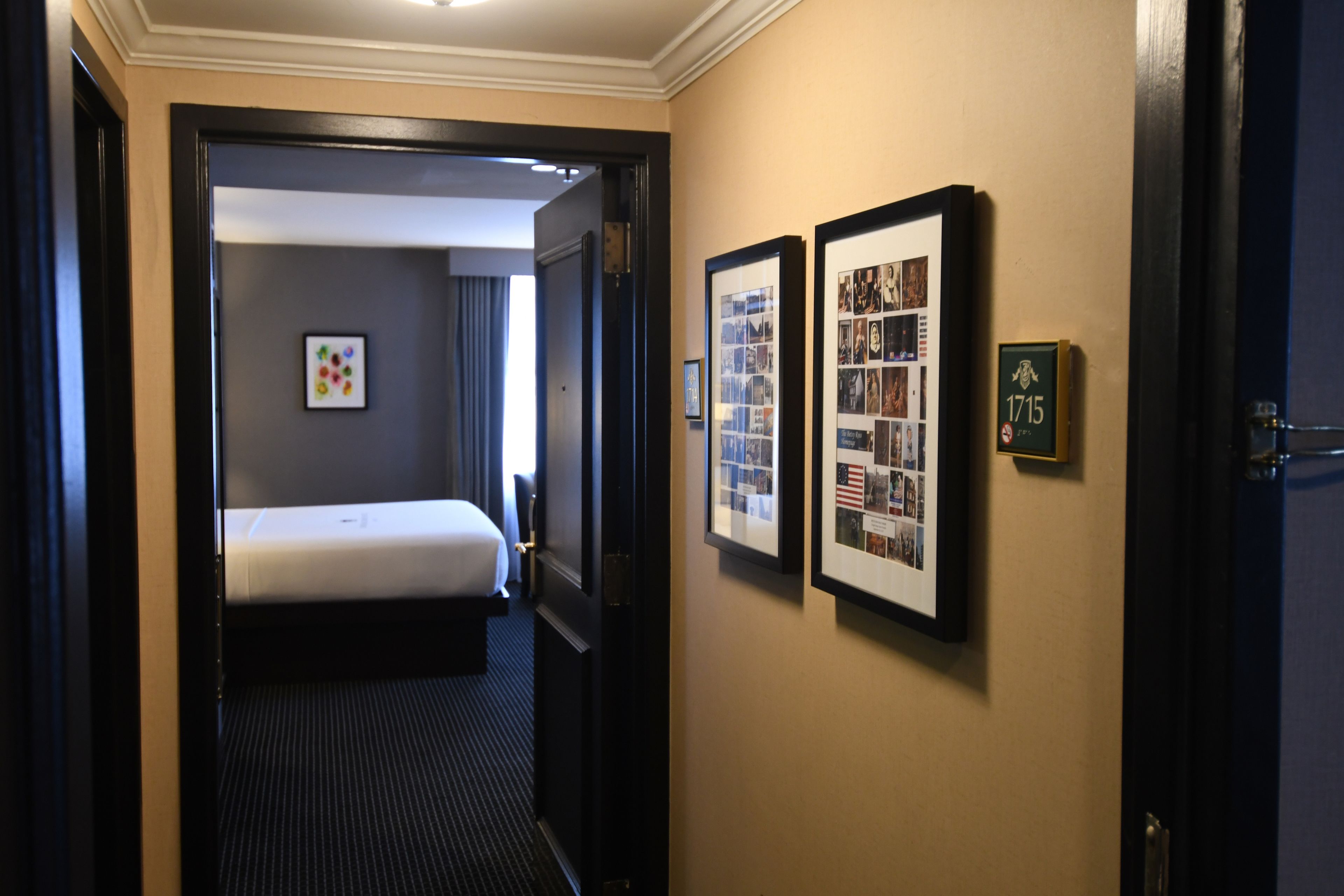 A hotel room with a bed, a framed collage of photos on the wall, and a door with a number plaque.