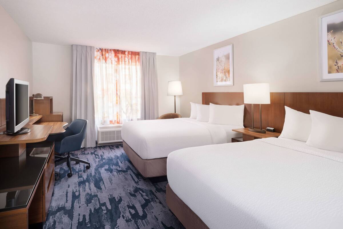 A hotel room with two beds, a desk with a computer, a chair, and a TV.